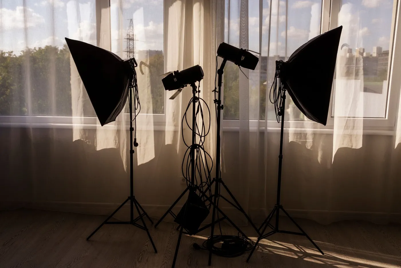 Two softboxes and two studio lights with barn doors on stands, silhouetted against a bright window
