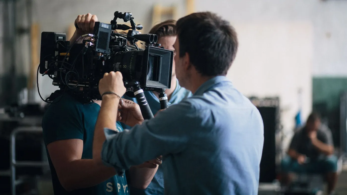 Film crew operating a cinema camera rig with a matte box and follow-focus on a warehouse set